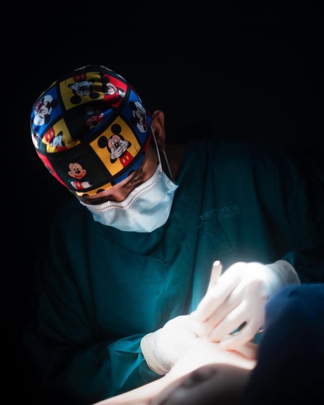 Dr. Andrés Iriarte durante una cirugía, con gorro quirúrgico estampado y luz dirigida